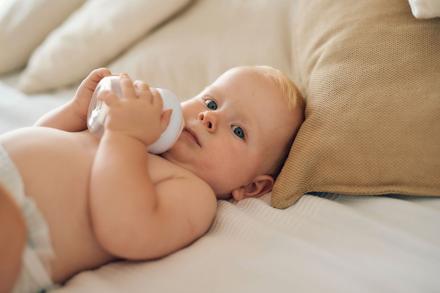 Beba leži na krevetu i pije mlijeko iz bočice