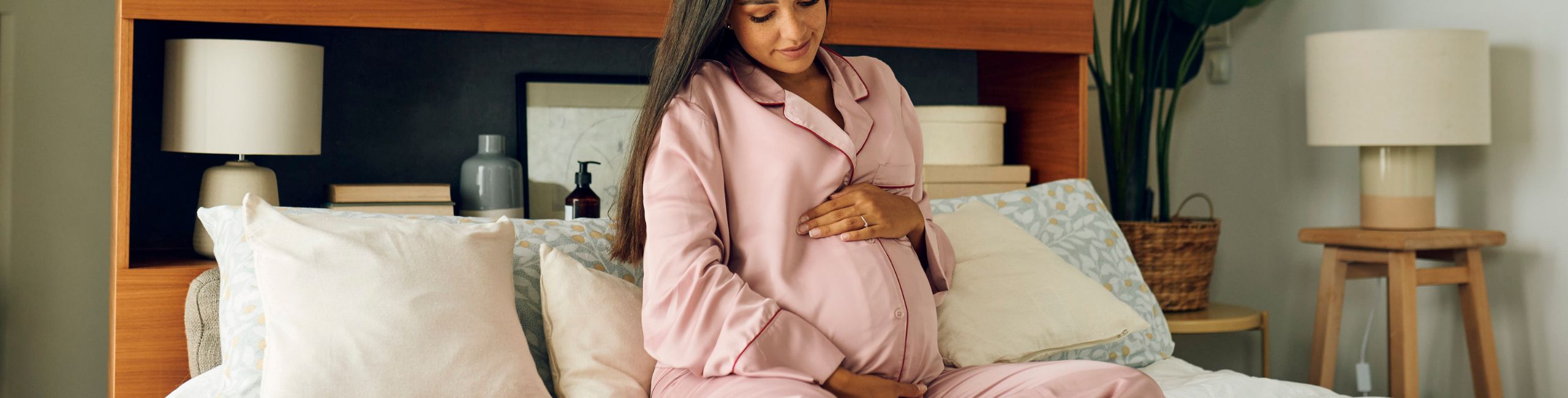 Trudnica sjedi u krevetu i dodiruje svoj trbuh - važnost vitamina u trudnoći