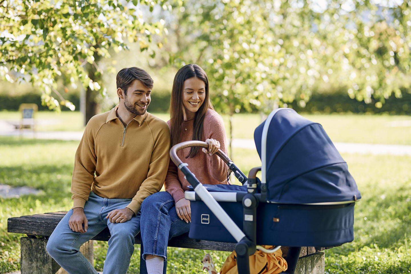 Roditelji s kolicima sjede na klupi u parku.