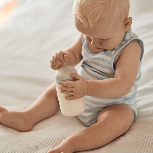 Beba sjedi na krevetu s bočicom Novalac mlijeka.