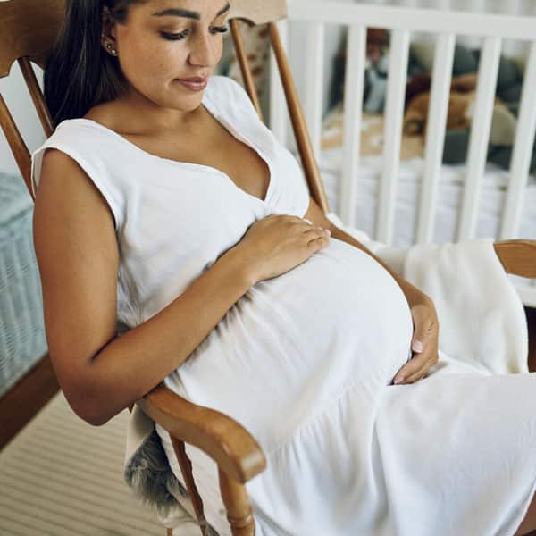 Trudnica sjedi na stolici i miluje svoj trbuh.