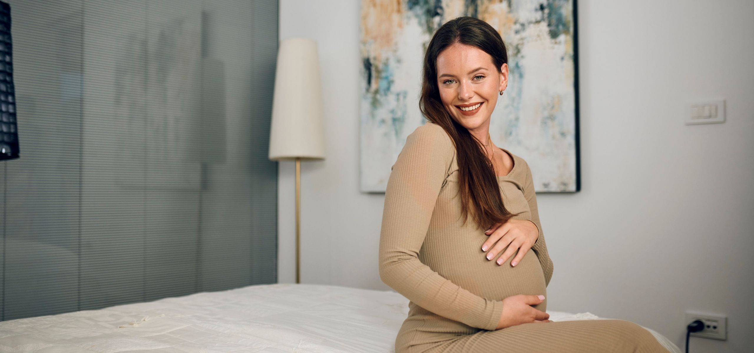 Trudnica sjedi na krevetu i miluje svoj trbuh