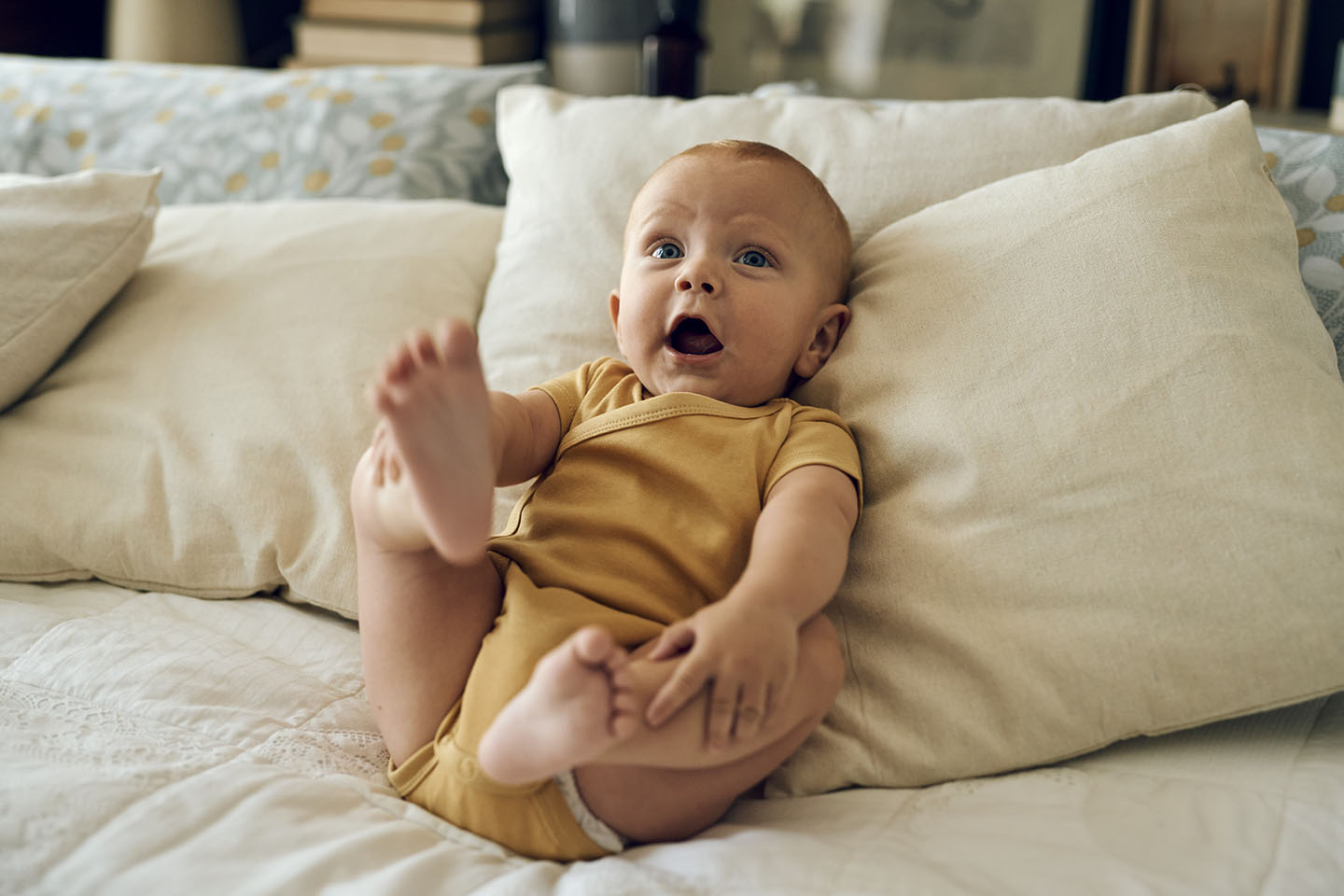 Beba sretno leži na jastucima i diže nožice.