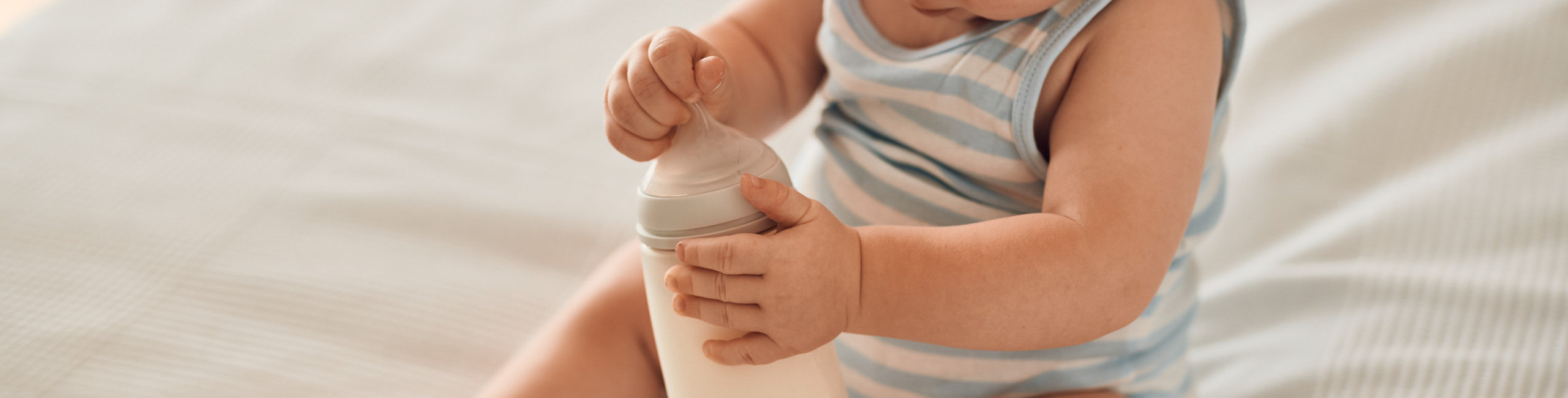 Beba sjedi na krevetu i drži bočicu u rukama.