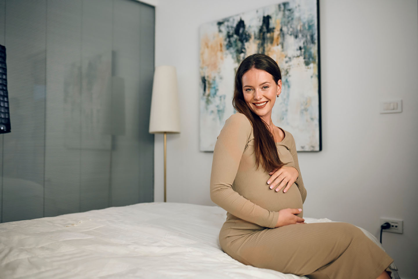 Trudna žena sjedi na krevetu i smiješi se